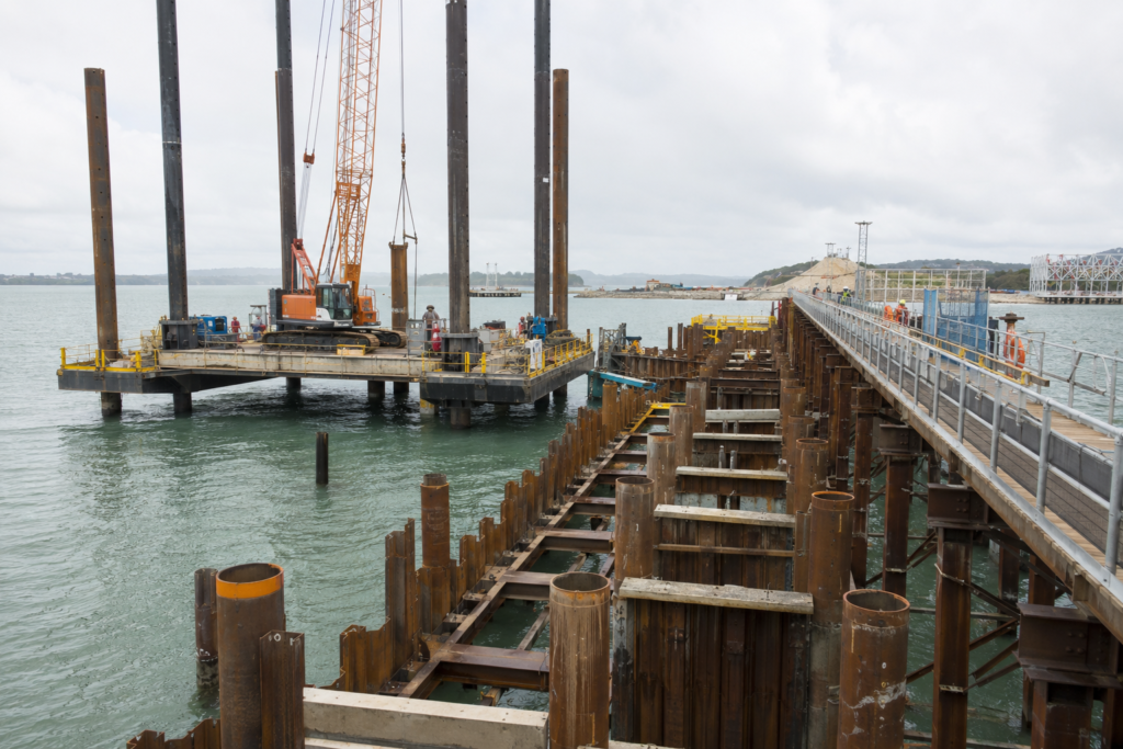 Marine construction site showing jack-up barge, temporary access trestle, and driven steel piles during jetty construction