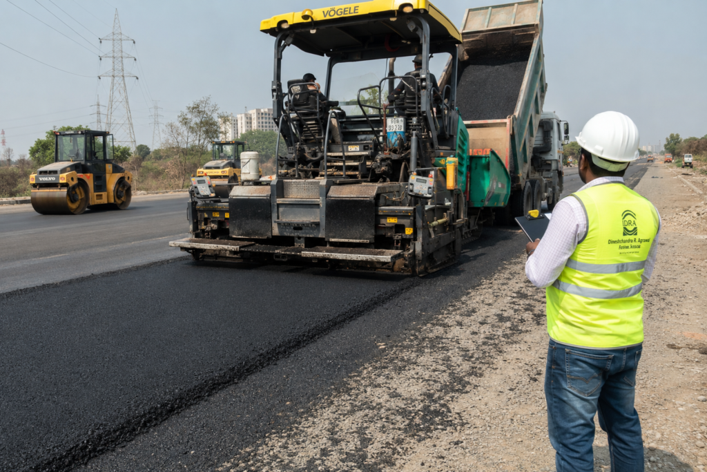 Road construction site showing asphalt paver laying wearing course with compaction roller following behind during road building operation