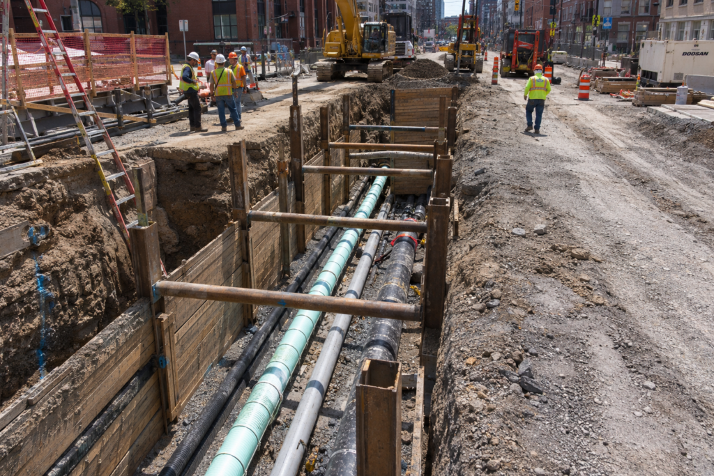Urban infrastructure construction site showing multi-utility trench with stormwater and foul sewer pipe layers in an active city environmen